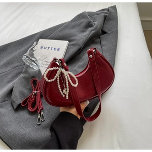 Detail of red patent leather crescent bag with pearl bow charm on a grey suit jacket