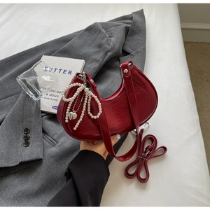 Detail of burgundy patent leather crescent bag featuring pearl bow and silver heart charms
