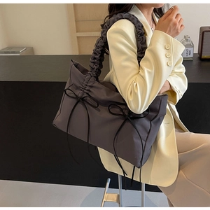 Detail van donkergrijze nylon schoudertas met geplooide handvaten en zwarte lintstrikken