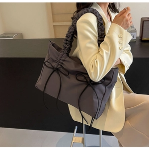 Detail van schoudertas met zwarte strikken en geplooide riem op grijs nylon materiaal