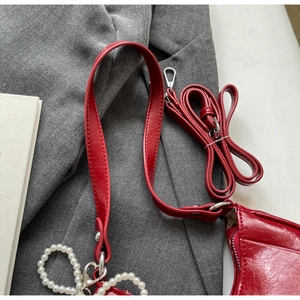 Close-up of red leather handbag texture with pearl charm and silver hardware accents