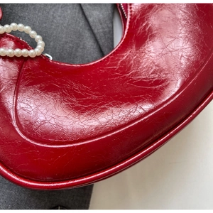 Detail of red wrinkled patent leather hobo bag featuring large white pearl handle