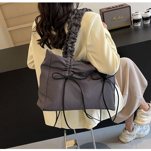 Detail van grijze nylon draagtas met geplooide handgreep en decoratieve zijstrikken