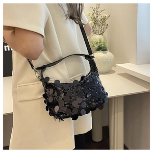 Detail view of black sequin shoulder bag with leather strap worn by a model