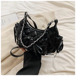 Detail of black quilted shoulder bag with chain tassel and bow on white bedding