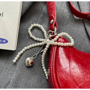 Detail of red crinkled leather bag with pearl bow and silver heart pendant charm