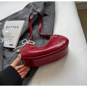 Detail of dark red crescent shoulder bag with polished leather and pearl accessory