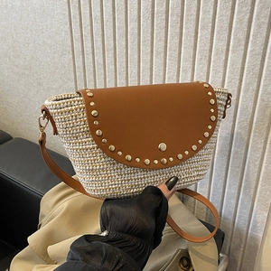 Woven straw saddle crossbody bag with brown leather flap and decorative metal rivets