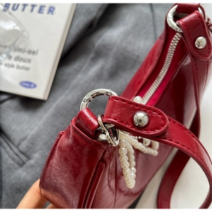 Detail of red patent leather shoulder bag featuring decorative pearl chain and silver hardware