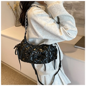 Detail of black quilted hobo bag featuring a decorative bow and silver chain strap