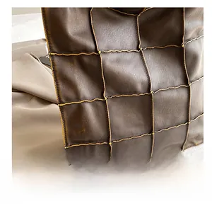 Detail of dark brown leather tote featuring grid stitching and yellow contrast thread