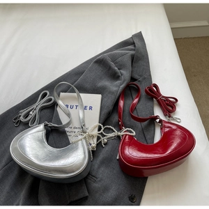 Detail of silver and burgundy crescent bags with pearl chains on a grey suit