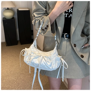 Detail of white quilted crescent bag with leather bows and silver chain strap on model