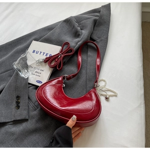 Detail of red crescent underarm bag with glossy patent leather and pearl chain decoration