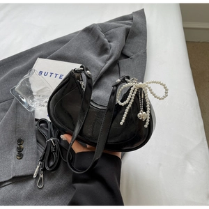 Detail of glossy black crescent bag with pearl bow and silver heart charm on blazer