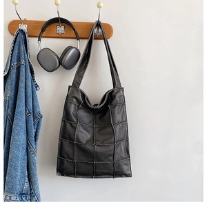 Detailed view of black quilted tote bag with white stitching hanging in a lifestyle setting
