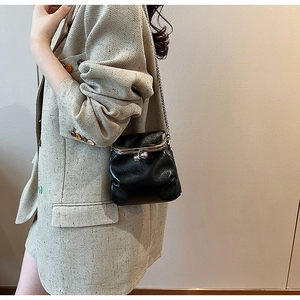 Détail d'un sac à fermoir rétro en cuir noir avec chaîne argentée porté sur une robe beige