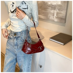 Détail du sac croissant en cuir verni rouge avec œillets argentés et boucles en métal