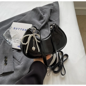 Close-up of black glossy crescent bag with pearl bow charm and silver hardware detail