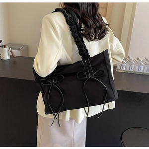 Detail van zwarte nylon schoudertas met strikken en geplooide riem gedragen door model