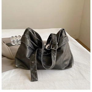 Detail of black matte leather shoulder bag with wide buckled strap and silver metallic holes