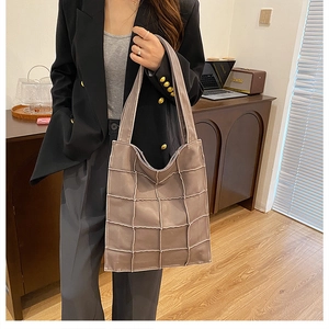 Detail of a large brown quilted tote bag styled with a professional black blazer