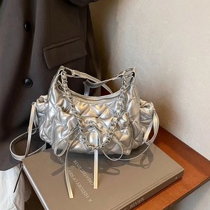 Quilted silver hobo bag with chain strap and drawstring design on a book background