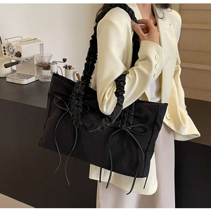 Detail van zwarte nylon draagtas met wit gestikte strikken en geplooide schouderband