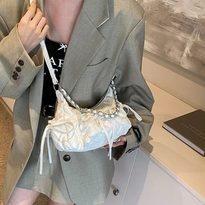 White quilted shoulder bag with silver chain and bow detail, worn by a model in a suit