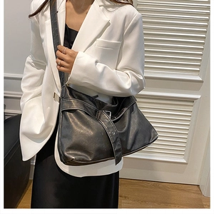 Close-up of black leather tote bag with wide shoulder strap and metal buckle detail