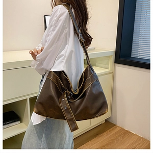 Detail of vintage brown leather tote bag with wide strap on model in cozy interior
