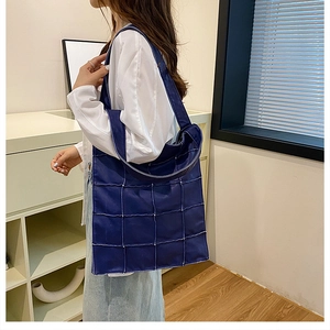 Close-up of deep blue quilted faux leather tote bag with square stitching and glossy finish