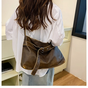Detailed view of vintage brown leather shoulder bag with silver buckle worn by a model