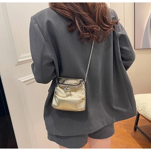Mini metallic gold chain crossbody bag shown on model wearing a grey suit in a modern setting