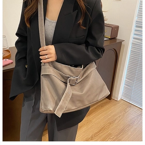 Detail of taupe leather shoulder bag with buckle strap on a black blazer model
