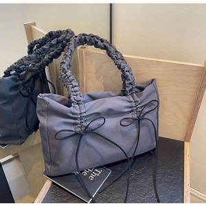 Detail van grijsblauwe nylon draagtas met geplooide handvatten en zwarte strikaccenten