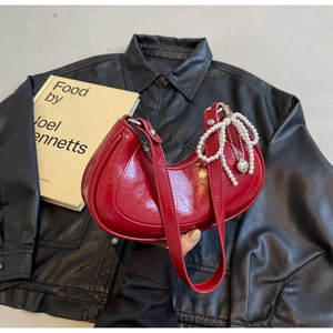 Detail of red crescent shoulder bag with glossy finish and pearl bow charm accessory
