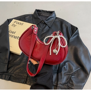 Detail of red patent leather crescent bag with pearl bow and silver heart charm