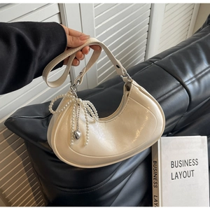 Detailed shot of beige half-moon bag featuring pearl bow and metallic heart pendant