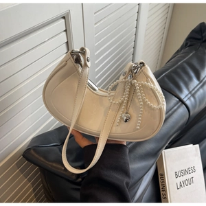 Close-up of creamy off-white leather crescent bag with pearl bow and silver heart pendant