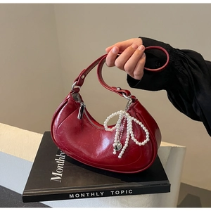 Close-up of wine red crescent bag with pearl bow charm and silver heart pendant