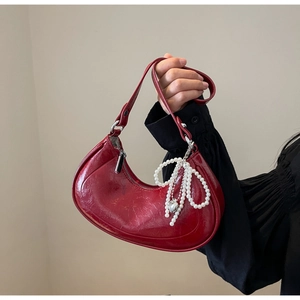 Detail of dark red half-moon bag with glossy texture and pearl bow charm accessory