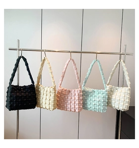 Detail of five cream puff style shoulder bags in varied colors on a minimalist metal rack