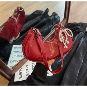 Detail of red crescent bag with glossy crackle leather and pearl bow charm decor