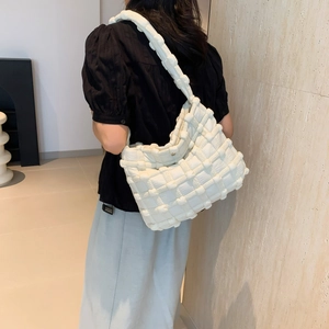 Detail of quilted puffy shoulder bag in cream white worn by model in minimalist setting