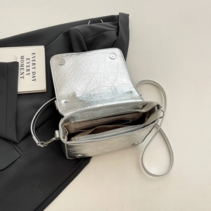 Silver metallic crossbody bag with textured pleats and multi-layer storage on black suit