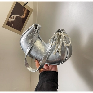 Detail of silver hobo bag featuring metallic texture and a pearl bow charm accessory