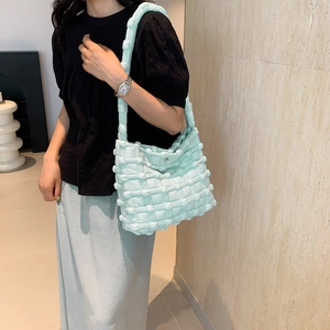 Close-up of light blue quilted shoulder bag with woven texture and wide strap
