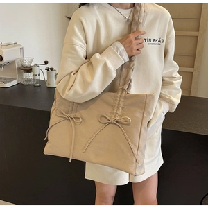 Detail van beige canvas draagtas met decoratieve strikken en een geplooide schouderband