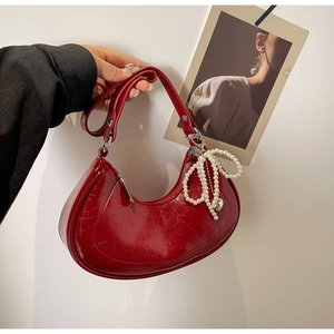 Detail of red patent leather saddle bag with pearl bow charm and vintage texture